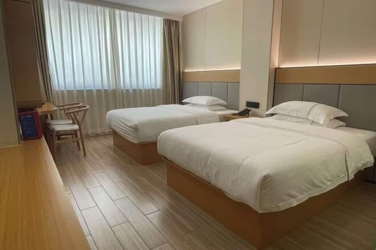 Habitación de hotel con dos camas, un escritorio, una silla y un ventanal con cortinas.