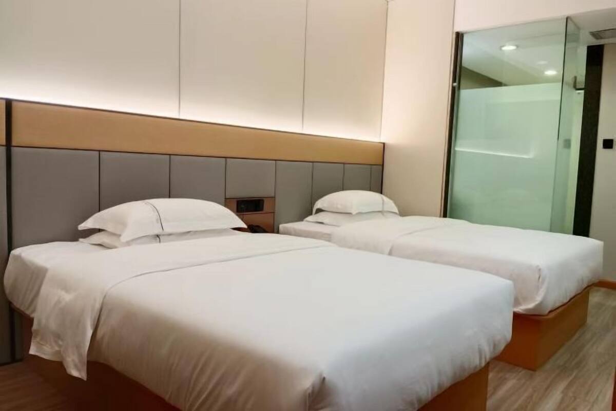 Habitación de hotel con dos camas, cabecera moderna, cabina de ducha de vidrio y suelo de madera.