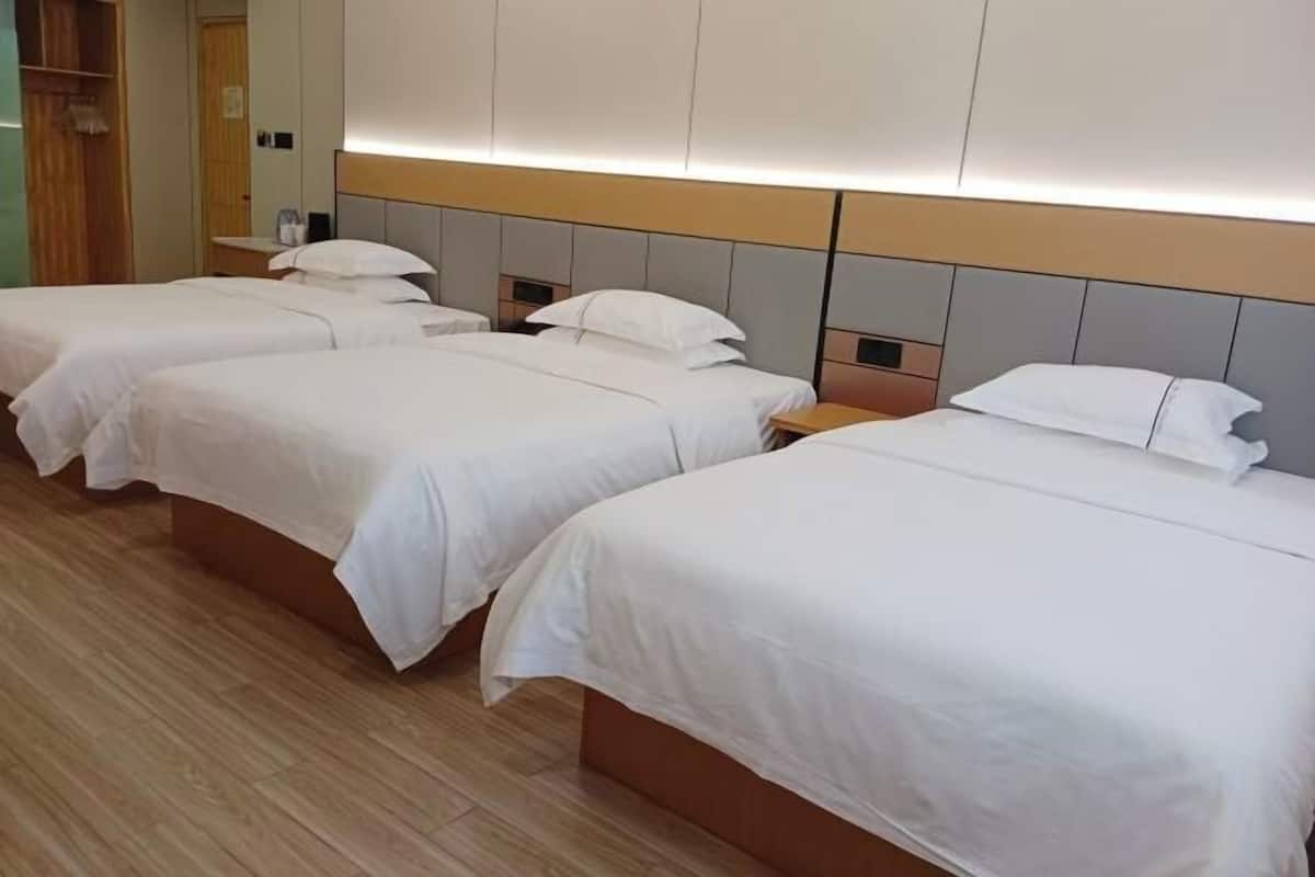 Habitación de hotel con tres camas individuales, suelo de madera y un espejo grande sobre las camas.