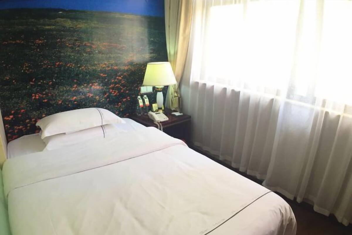 Habitación de hotel con una cama, una mesita de noche con lámpara y vistas al paisaje a través de la ventana.