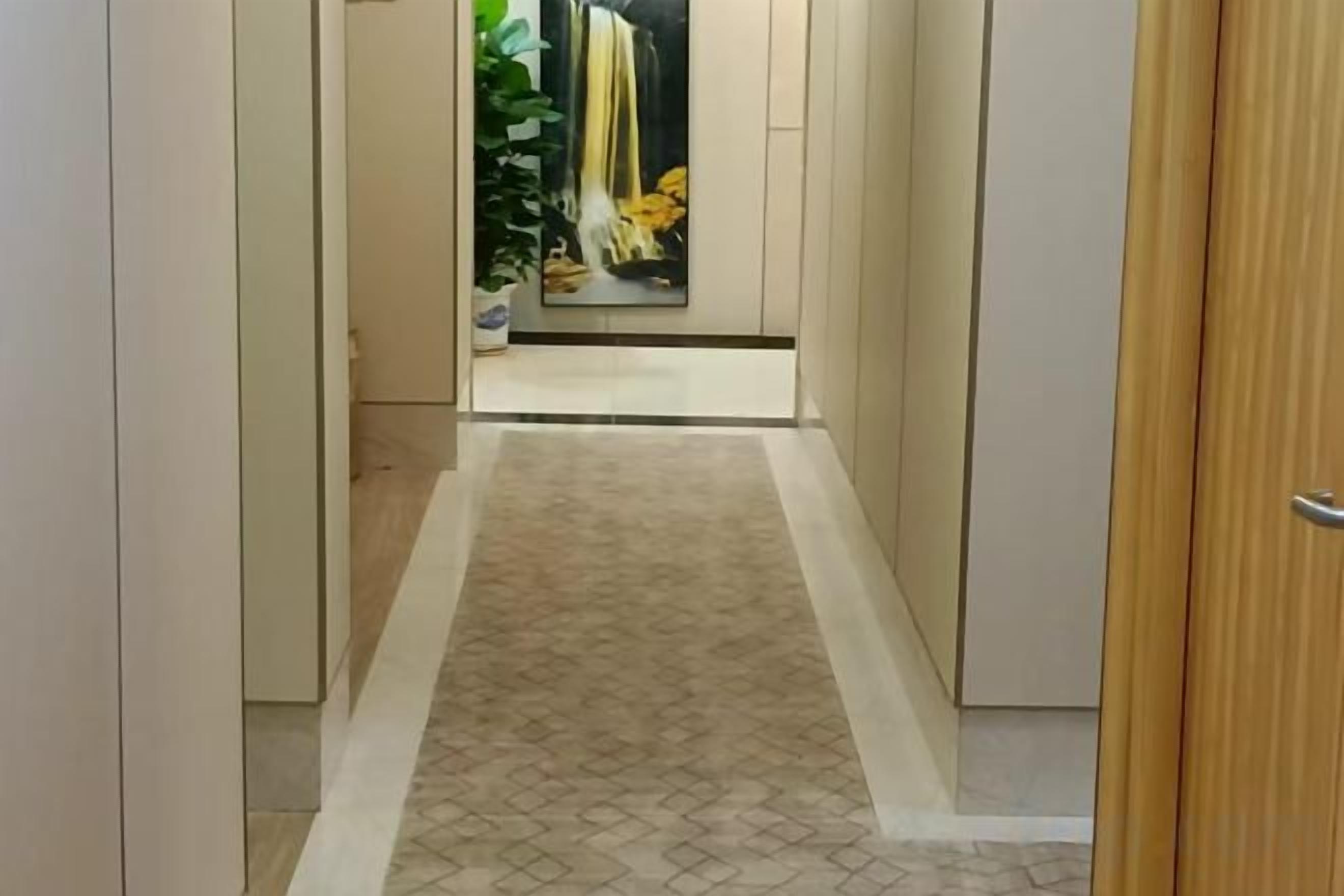 A hallway with a patterned carpet, a wooden door on the right, and a mirror reflecting a yellow curtain.