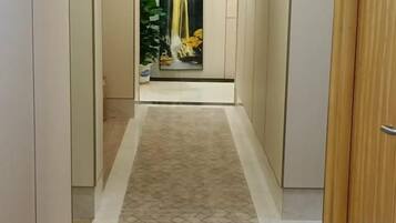 A hallway with a patterned carpet, a wooden door on the right, and a mirror reflecting a yellow curtain.