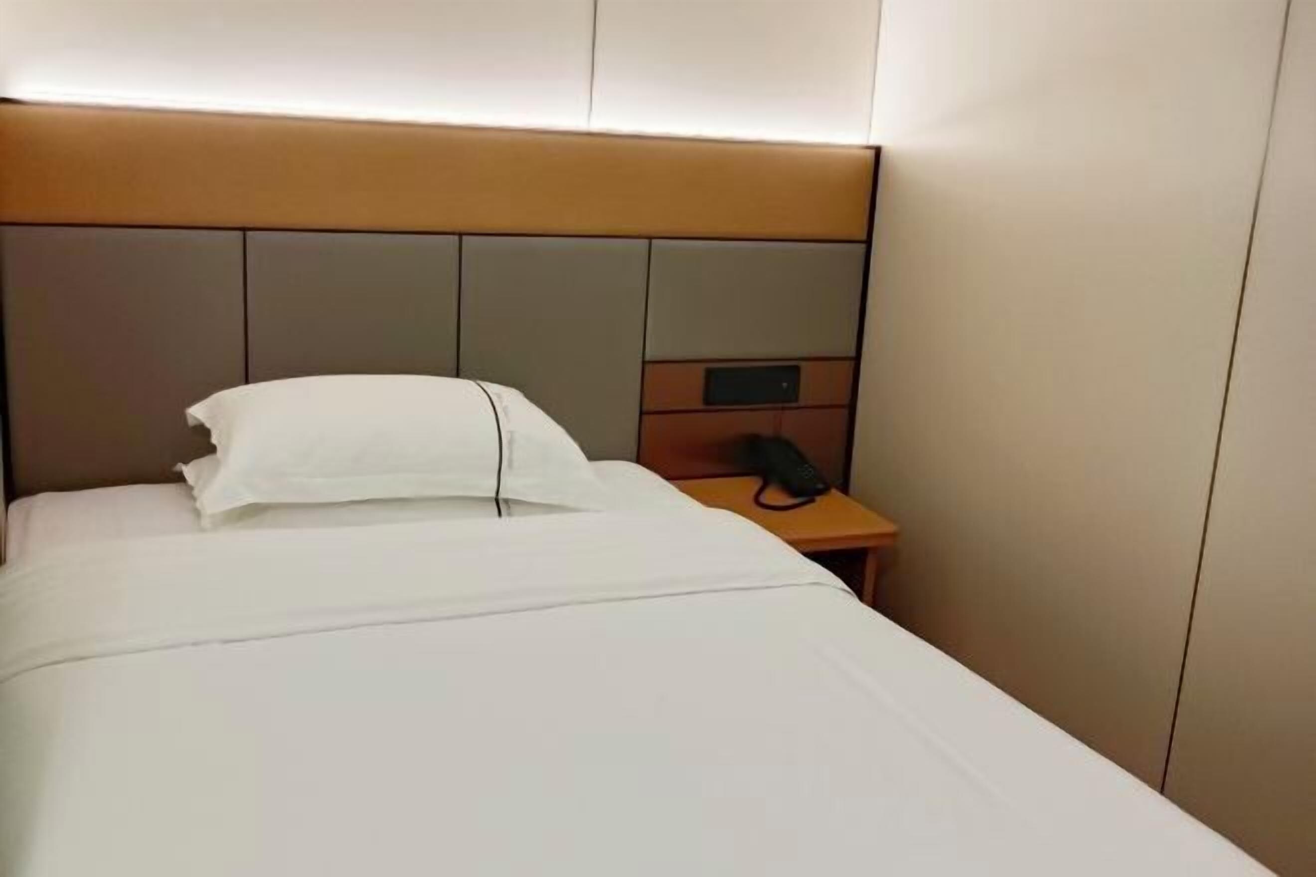 A hotel room with a bed, a bedside table with a phone, and a headboard with a control panel.