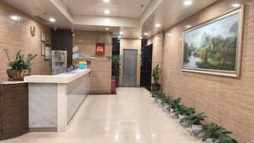 A hotel reception area with a reception desk, a clock, and a framed painting on the wall.