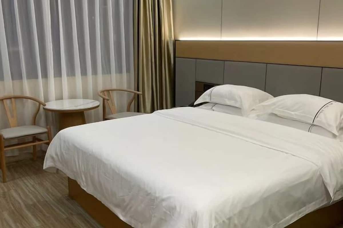 Una habitación de hotel con una cama, dos sillas, una mesita y una cortina.