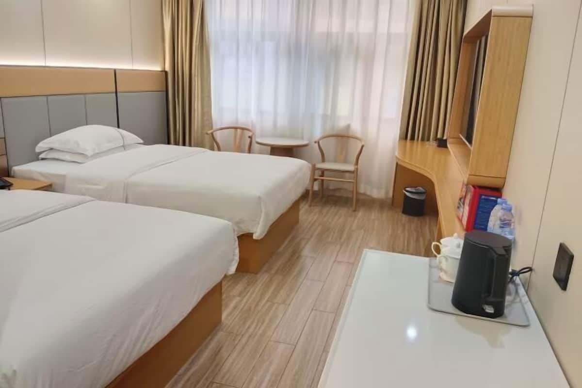 Habitación de hotel con dos camas, una mesita pequeña con cafetera, una silla y un televisor sobre un mueble de madera.