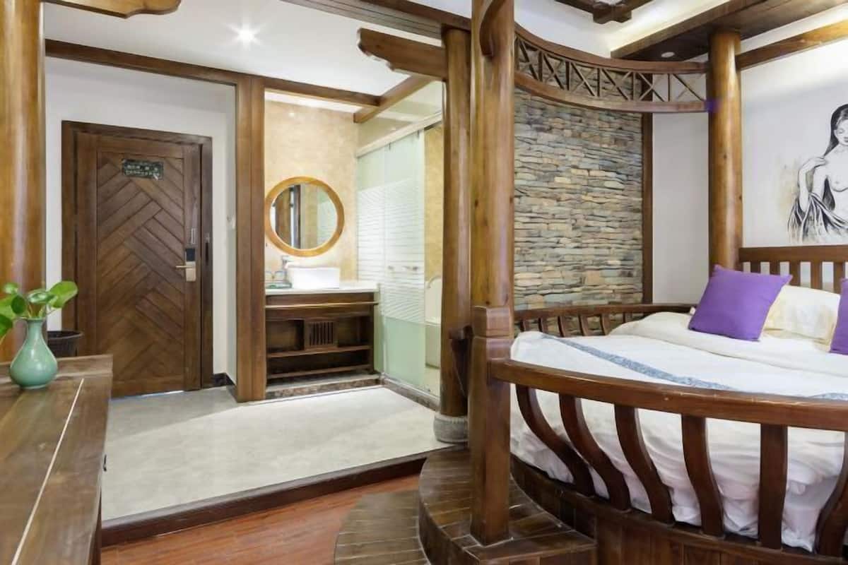 Une chambre à coucher avec un lit en bois, un mur en pierre, une porte en bois et une salle de bain équipée d’un lavabo et d’un miroir.