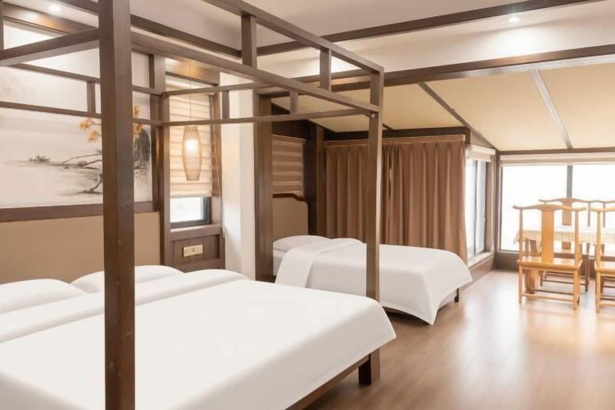 Une chambre d’hôtel avec trois lits, une structure de plafond en bois, un coin repas avec une table et des chaises, et une grande fenêtre.