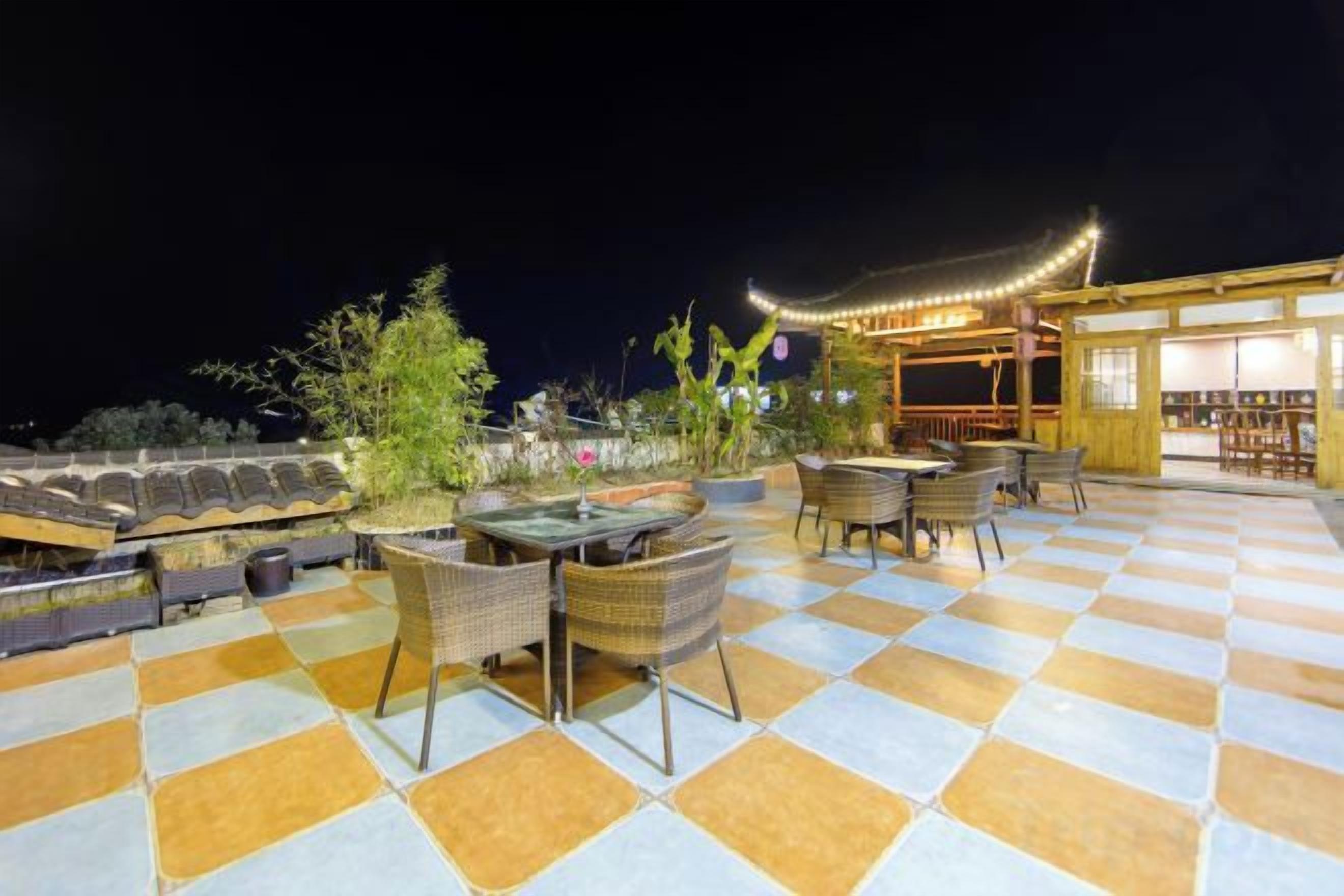 An outdoor seating area with tables and chairs, a checkered floor, and a building with a traditional architectural style in the background.