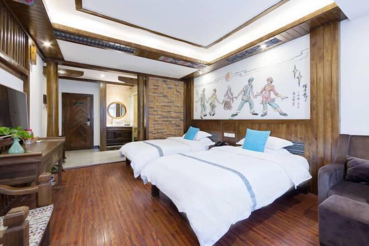 Une chambre avec deux lits, un plancher en bois, un mur en pierre servant d’élément décoratif, et une fresque représentant des personnes se tenant la main.