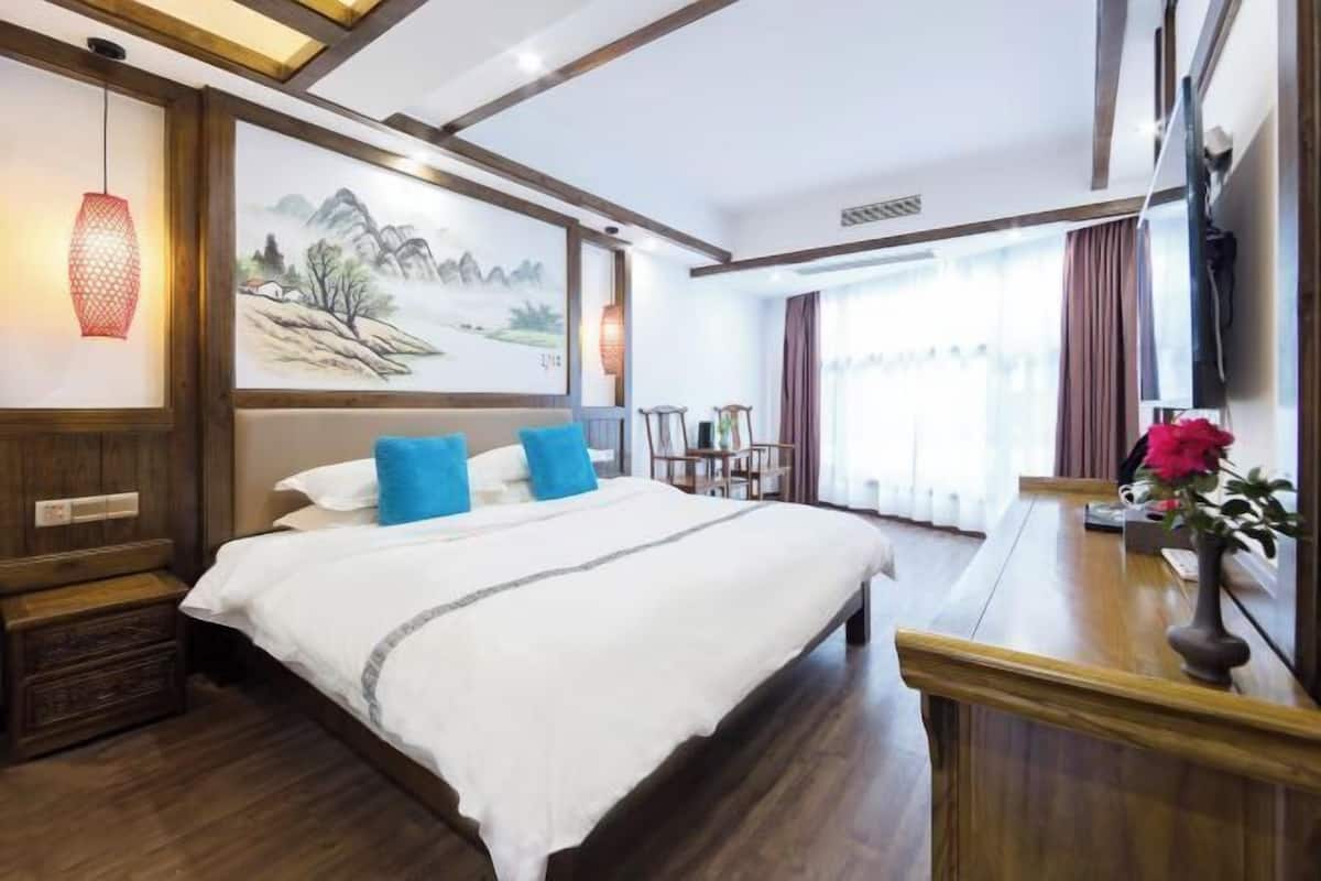 Une chambre d’hôtel avec un grand lit, une tête de lit en bois, un tableau au mur, un bureau agrémenté d’un vase de fleurs et un téléviseur fixé au mur.