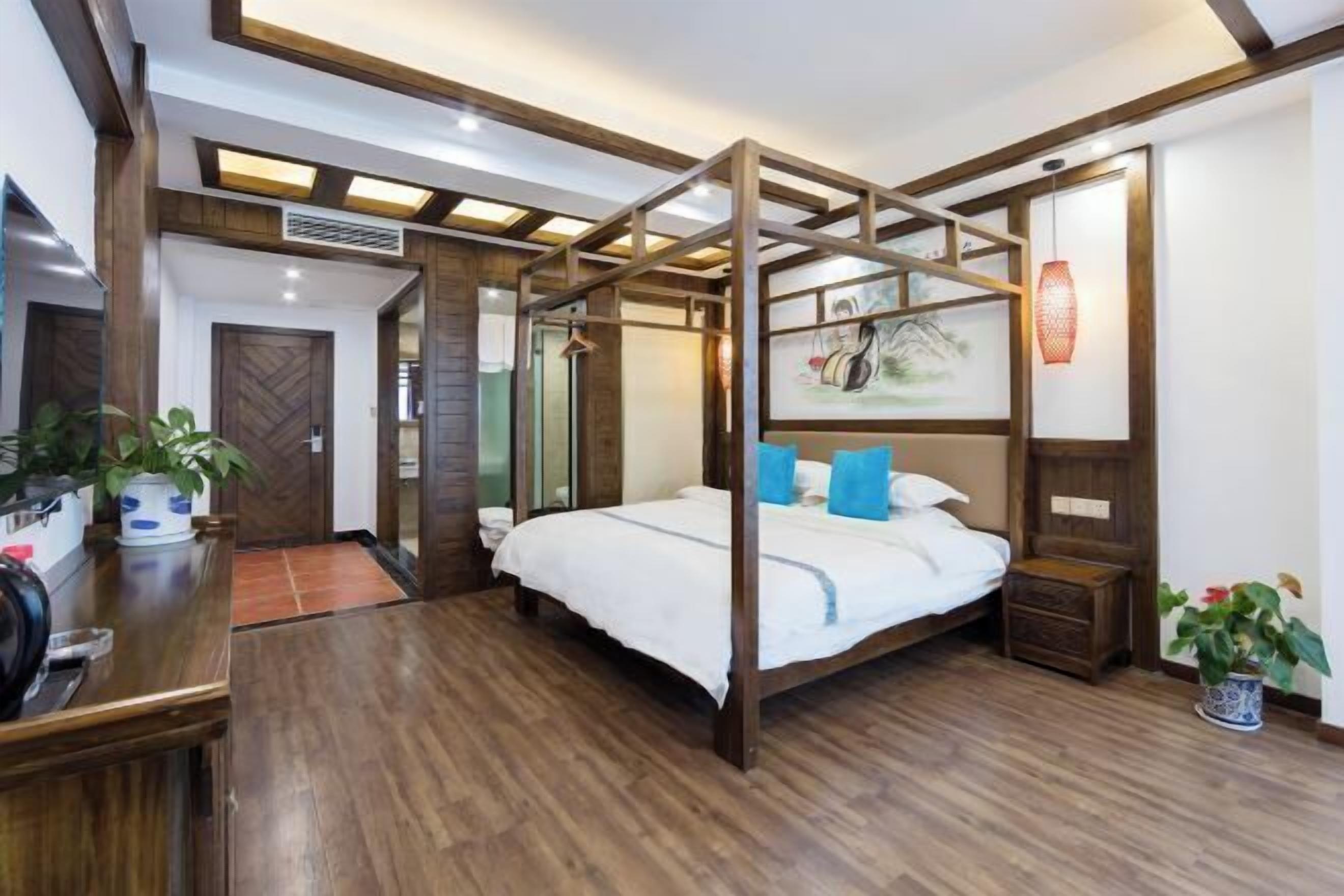 Una cama con dosel, con cubrecama blanco y almohadas azules, un escritorio de madera con una planta en maceta, y una repisa de pared con adornos.