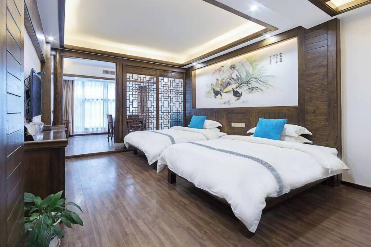 Une chambre d’hôtel avec deux lits, un plancher en bois, une télévision, un paravent décoratif et un tableau au mur.