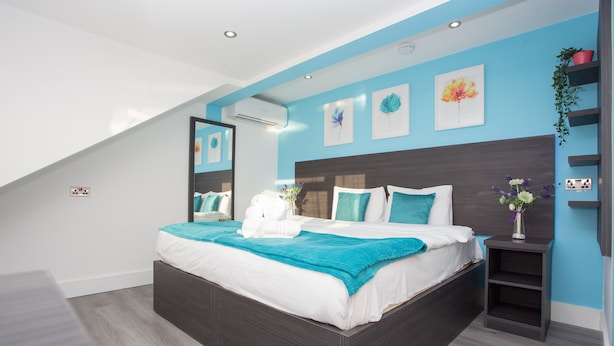 A modern bedroom with a large bed, a skylight, and a blue accent wall. - Heathrow Windsor Apart Hotel  (Slough)