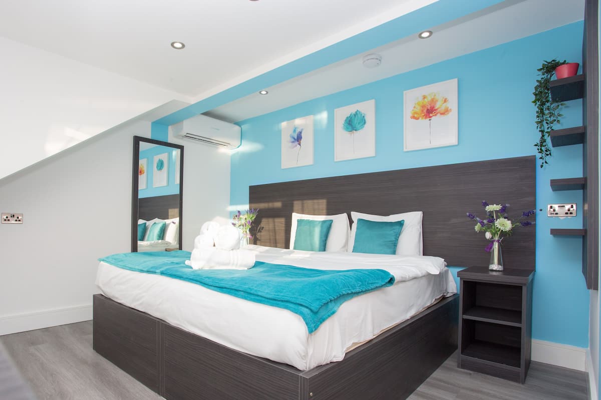 A modern bedroom with a large bed, a skylight, and a blue accent wall.