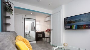 A modern living room with a sofa, a glass coffee table, and a mounted TV displaying various channels. - Heathrow Windsor Apart Hotel  (Slough)