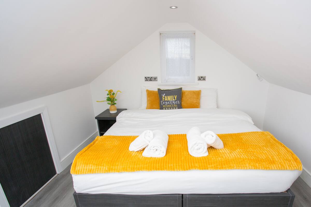 A bedroom with a bed, pillows, a nightstand, a vase with flowers, and a window.