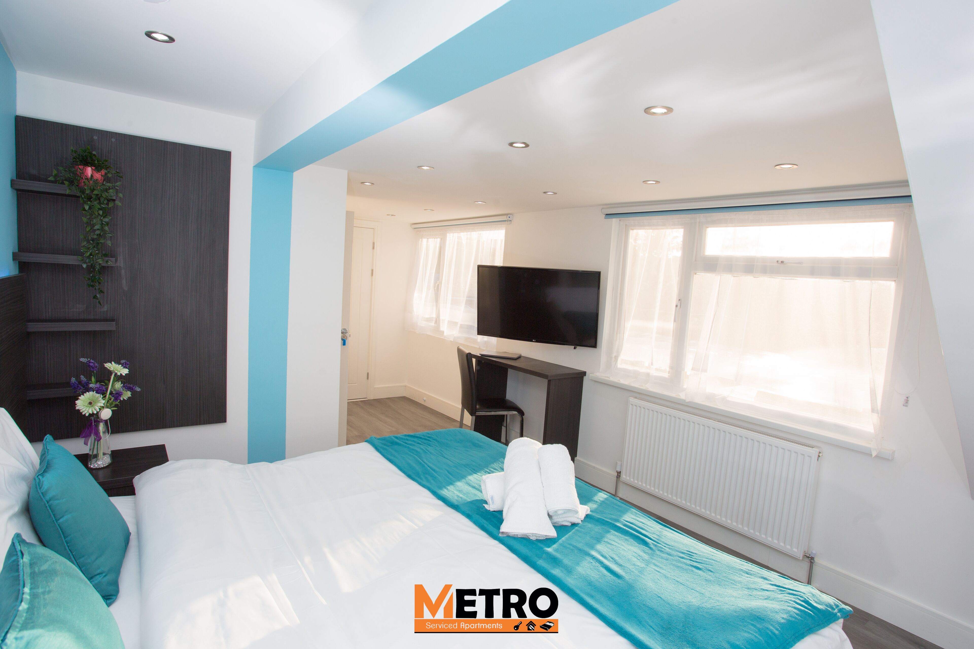 A modern hotel room with a bed, a desk, a TV, and a window with curtains.