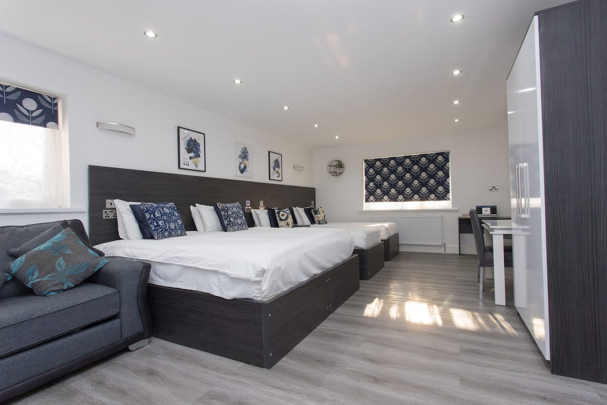A modern bedroom with a large bed, bedside tables, a sofa, and a desk.