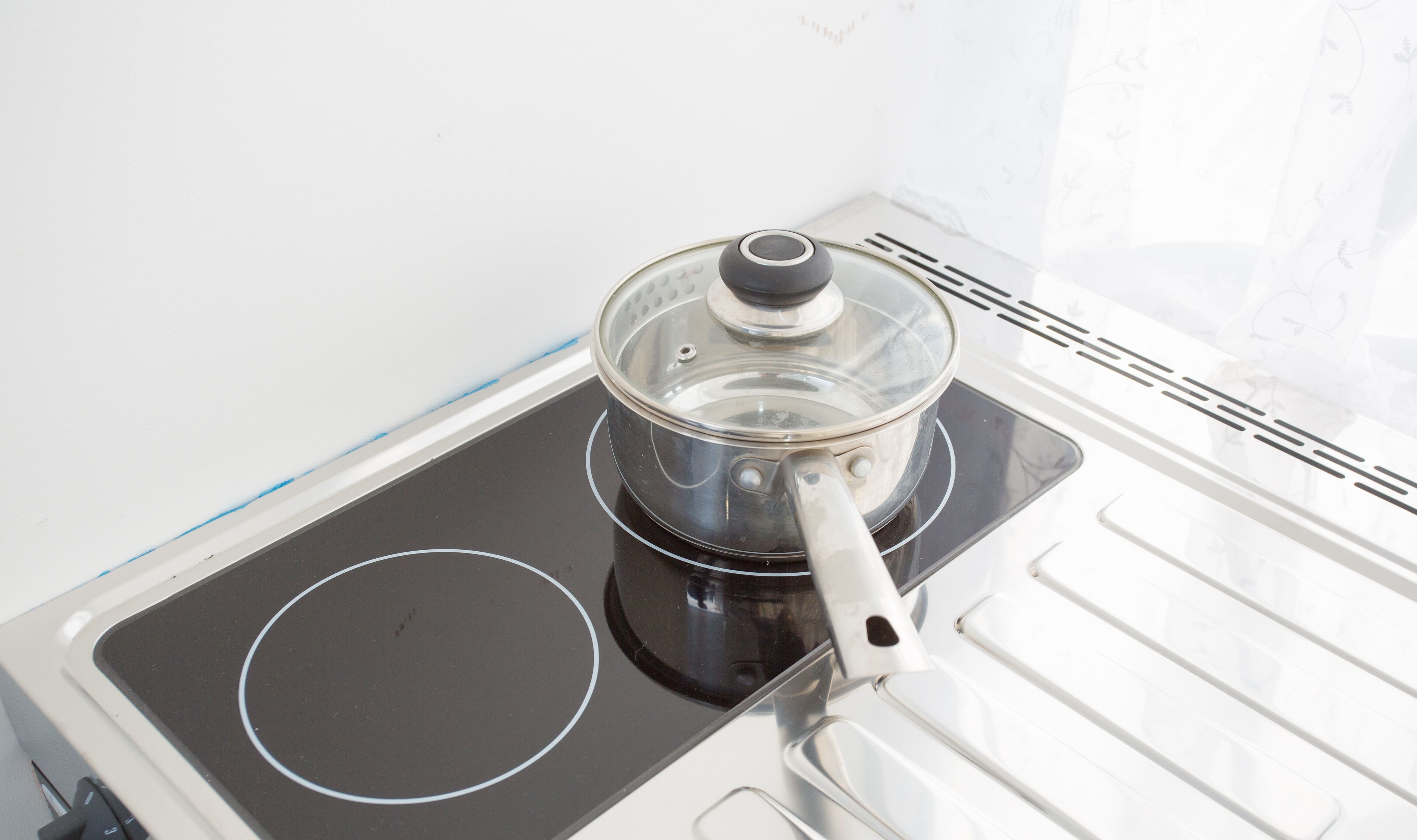 A kitchen with a stove, a pot on the stove, and a white wall with a subtle floral pattern.