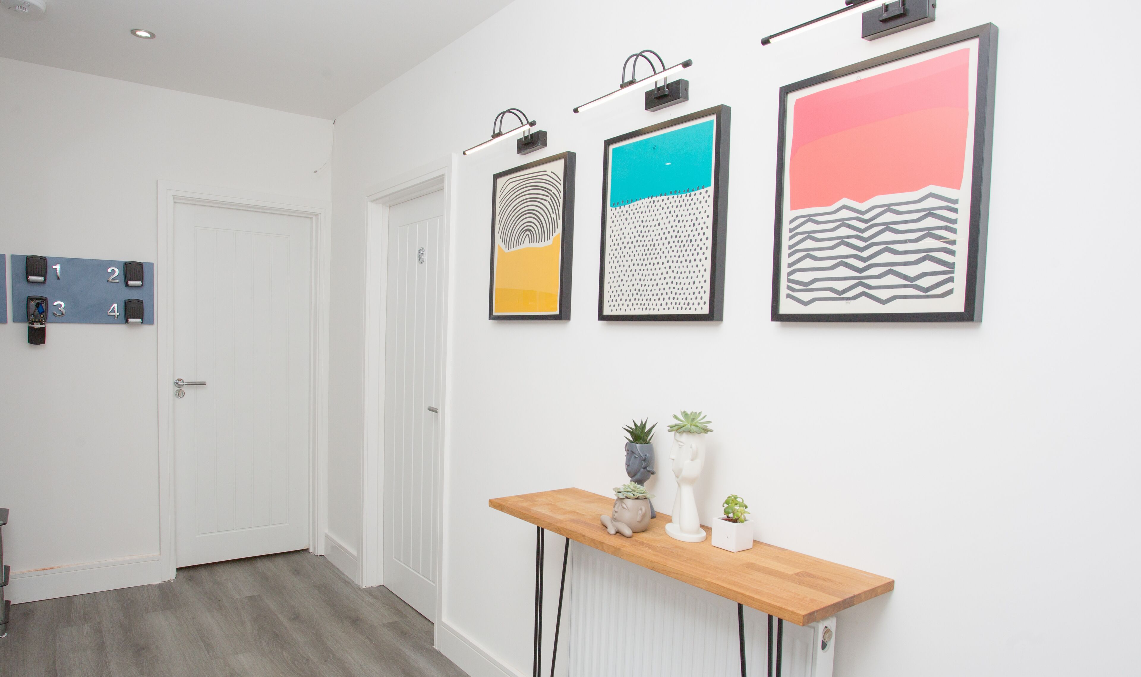 A hallway with a wooden console table, three framed artworks, and a door with numbered locks.