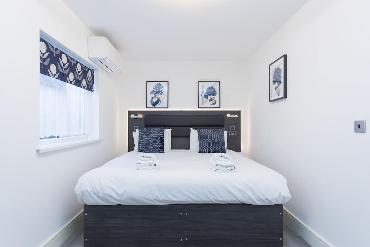 A modern hotel room with a large bed, a window with curtains, and two framed artworks on the wall.