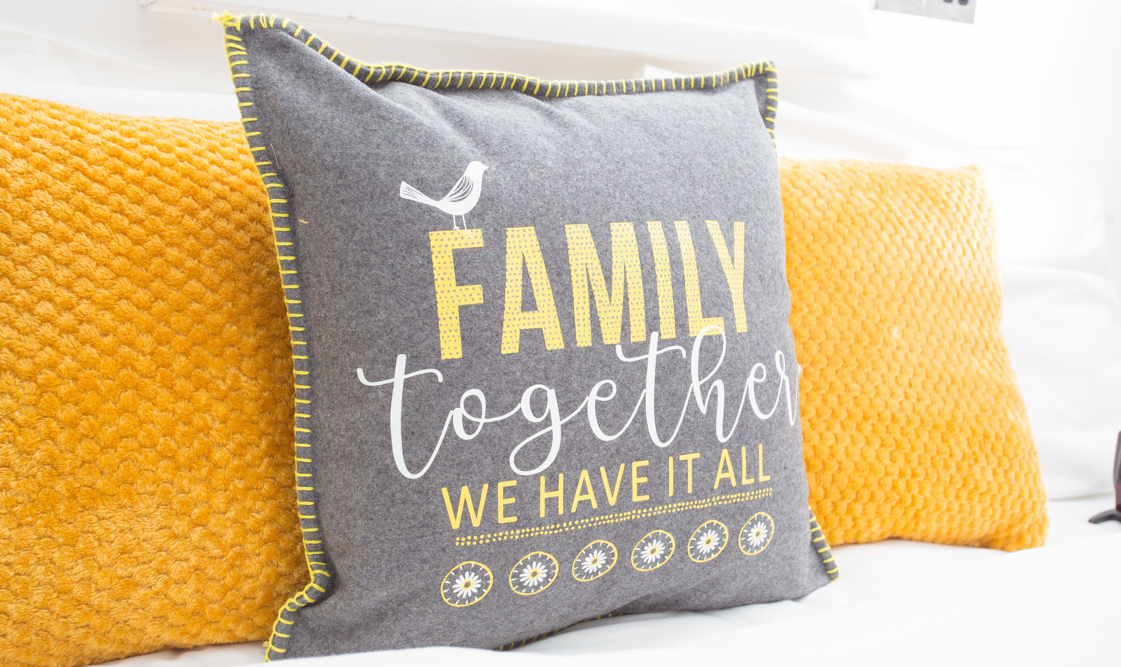 Un almohadón con el texto "FAMILIA unidos tenemos todo" sobre una cama con almohadones amarillos.