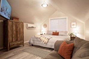 A bedroom with a bed, a wooden wardrobe, a ceiling light, a window with blinds, and a wall clock.