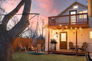 A two-story house with a porch, outdoor seating, and a swing set.