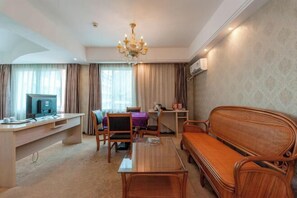 A hotel room with a wooden sofa, a coffee table, a desk with a computer, and a chandelier.