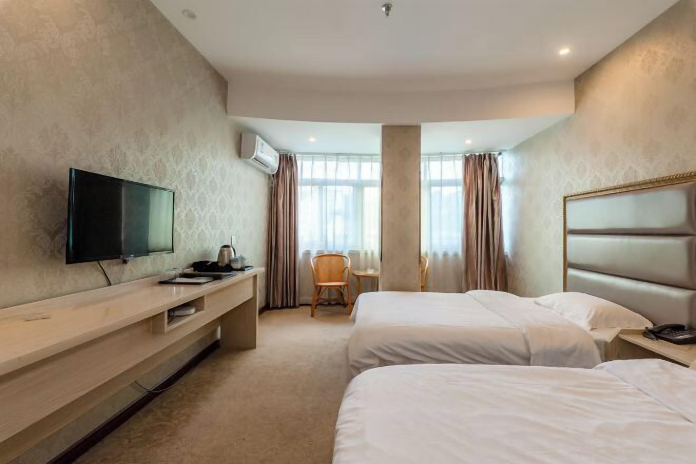 A hotel room with two beds, a TV, a desk, and a chair.