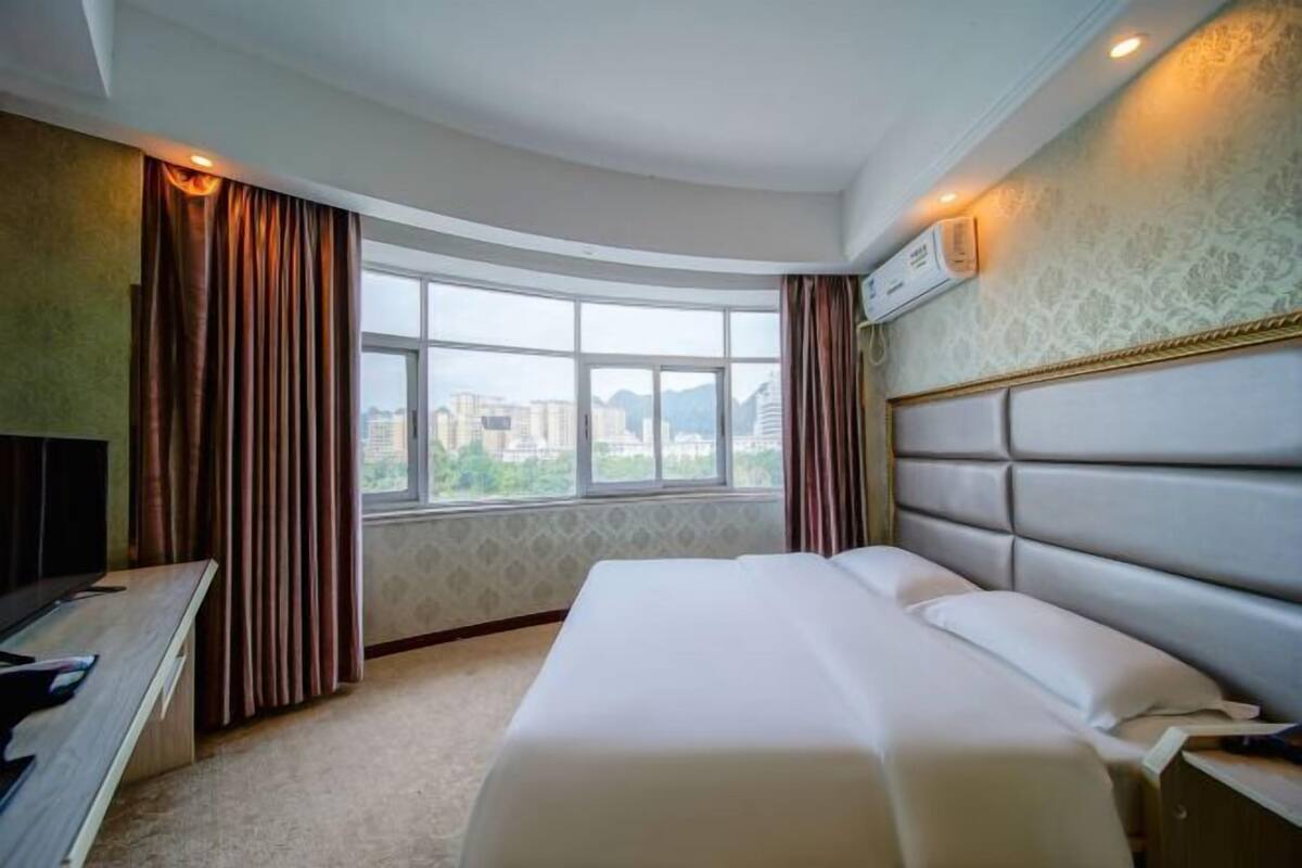 Een hotelkamer met een groot bed, een bureau met een computer en een raam met gordijnen.