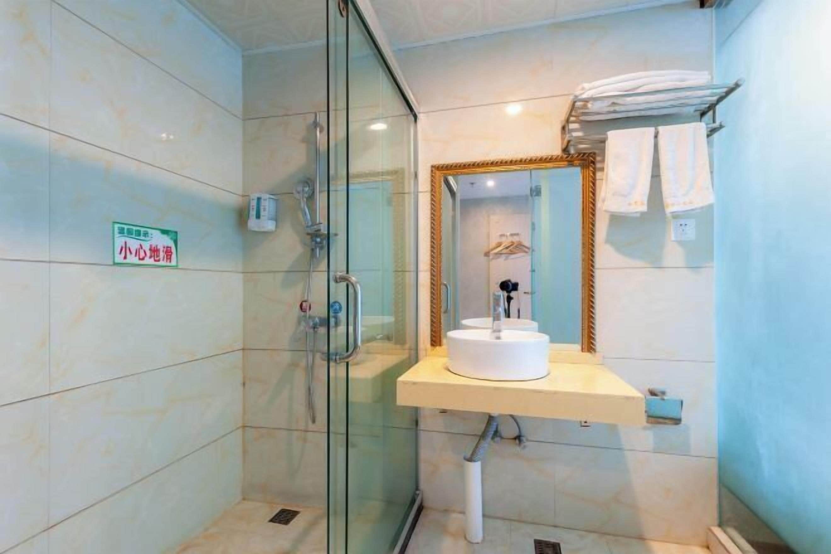 A modern bathroom with a glass-enclosed shower, a white sink with a mirror above it, and a towel rack with folded towels.