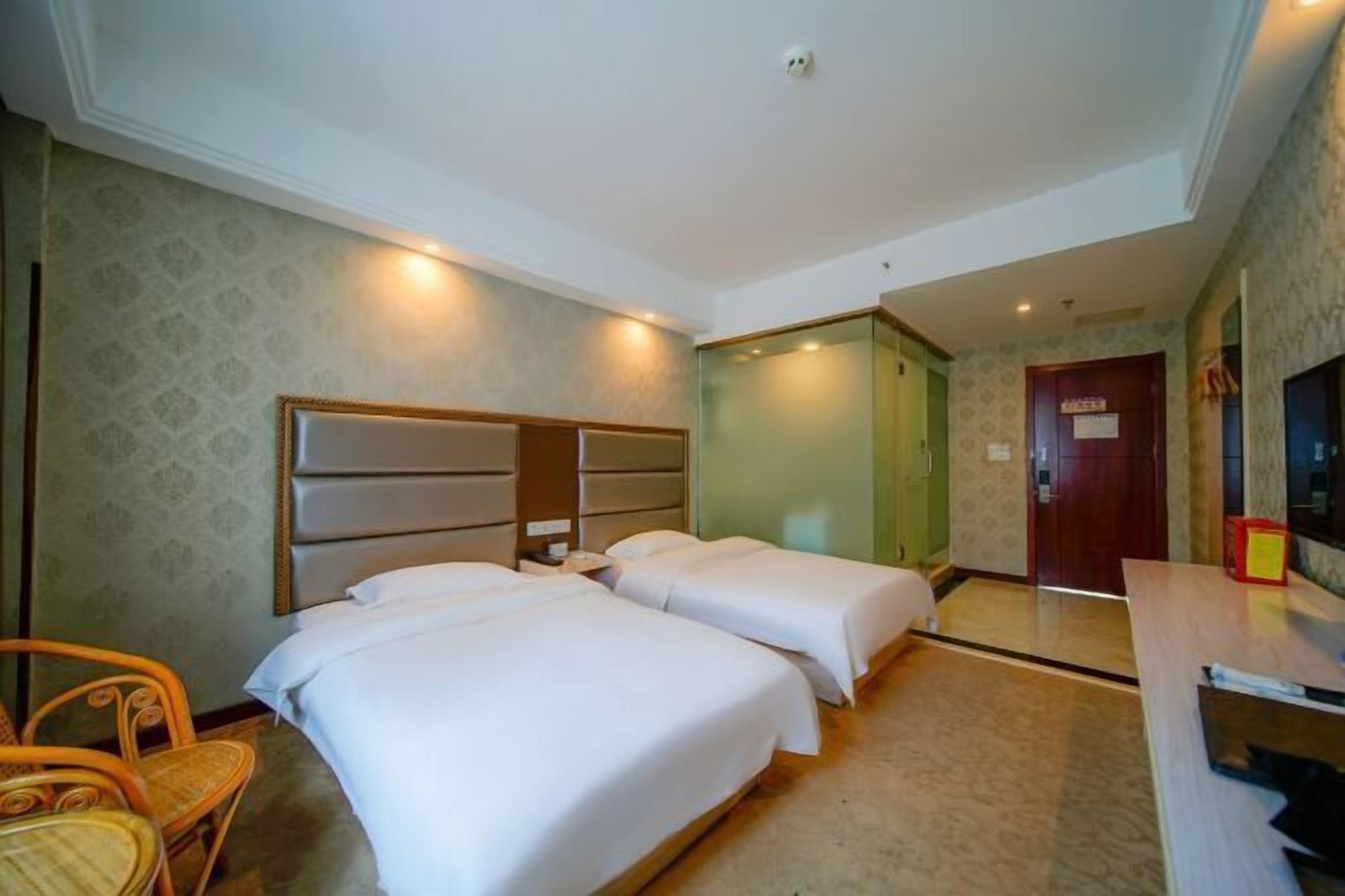 Ein Hotelzimmer mit zwei Betten, einem Schreibtisch, einem Sessel und einem Fernseher.