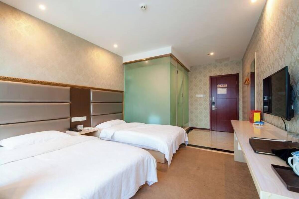 Een hotelkamer met twee bedden, een bureau, een televisie en een deur.