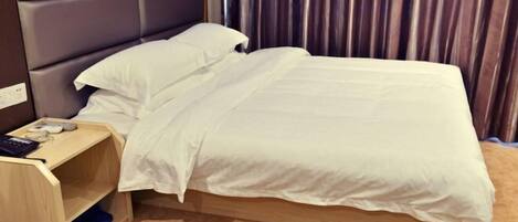 A neatly made bed with white bedding, a wooden nightstand with a phone and a book, and a headboard with a padded design.