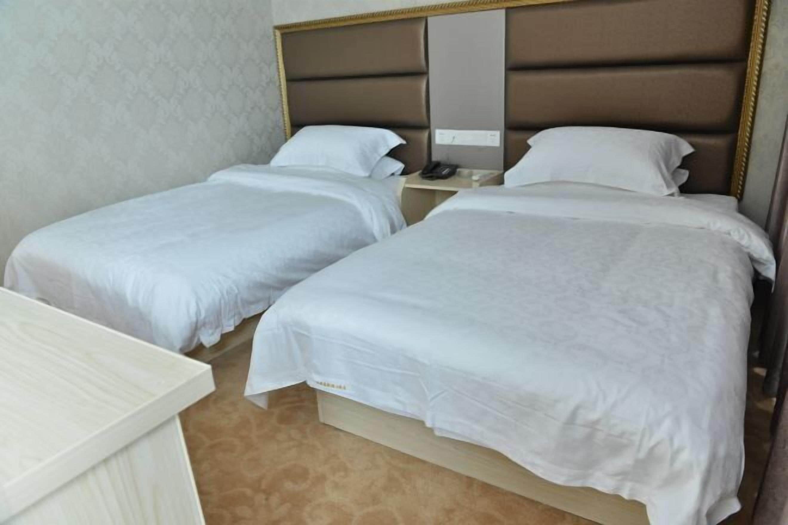 A hotel room with two single beds, a bedside table, a nightstand, and a wall-mounted phone.