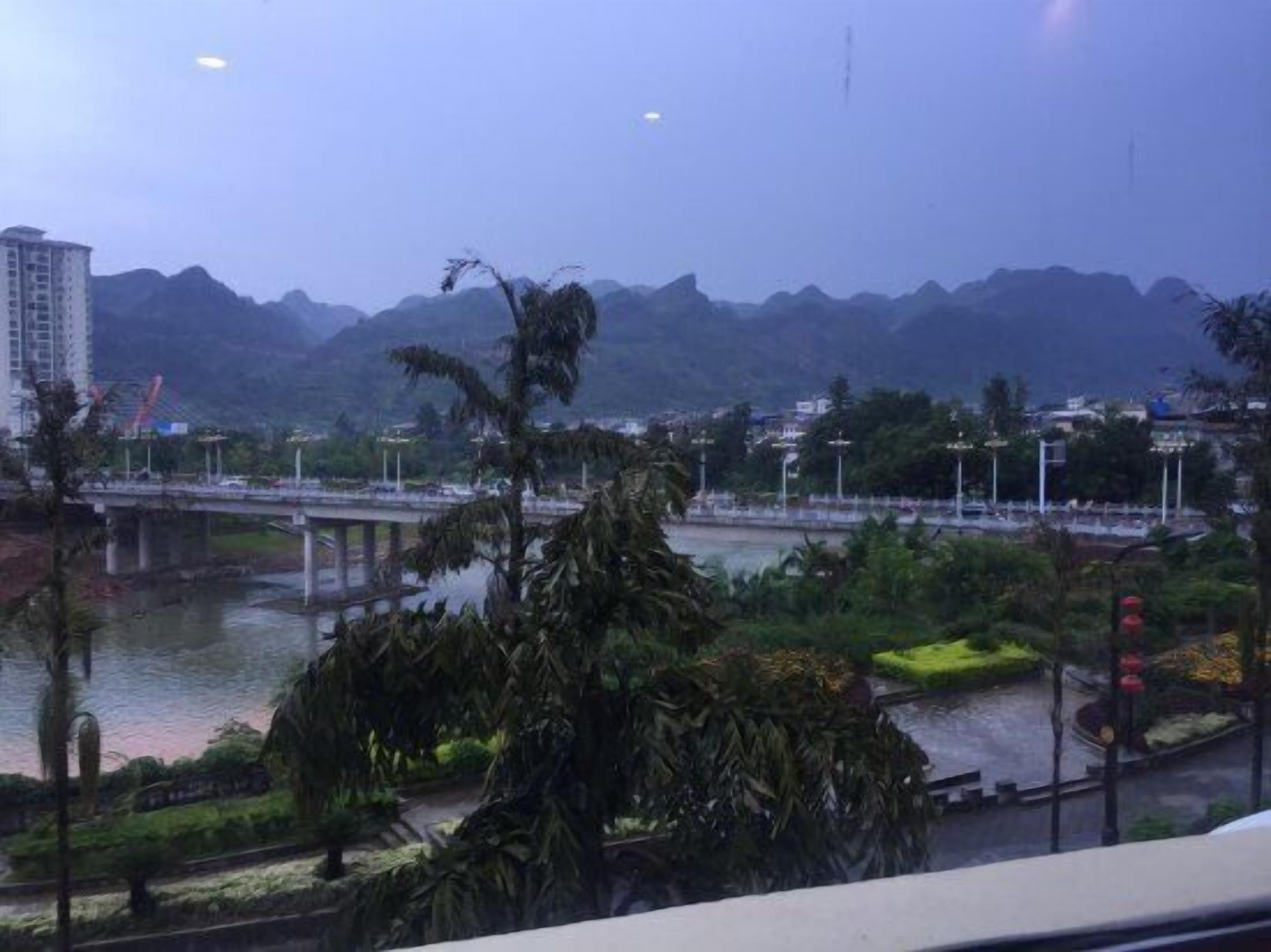 A view of a river with a bridge, mountains in the background, and some greenery in the foreground.