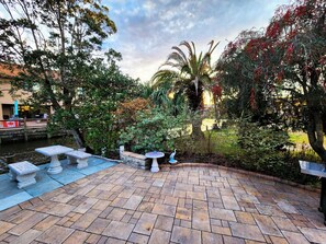 Un espacio de patio al aire libre con piso de piedra, un conjunto de asientos y diversas plantas.