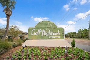 Schild für das Gulf Highlands Beach Resort, mit blauem Himmel und umgebender Vegetation.