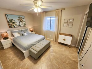 A bedroom with a bed, nightstands, a ceiling fan, a window with curtains, a bedside table, and a dresser.