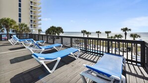 A wooden deck with blue lounge chairs overlooking a beach.