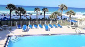 A pool area with lounge chairs and a view of the beach.