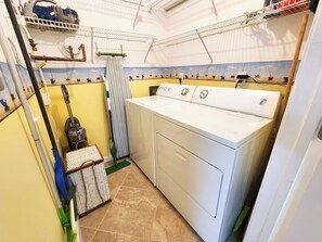 A laundry room with a large white washing machine, a striped drying rack, and a vacuum cleaner.