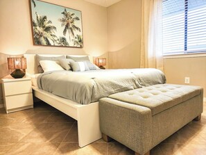Un dormitorio con cama, mesitas de noche, un banco y un cuadro en la pared.