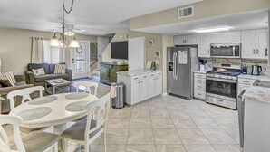 A modern kitchen with white cabinets, stainless steel appliances, and a dining area with a white table and chairs.