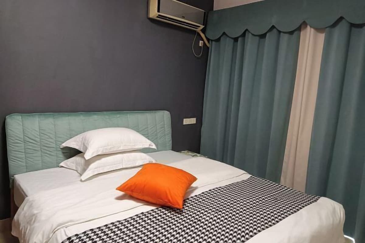 A neatly made bed with white and orange pillows, a patterned bedspread, and teal curtains.