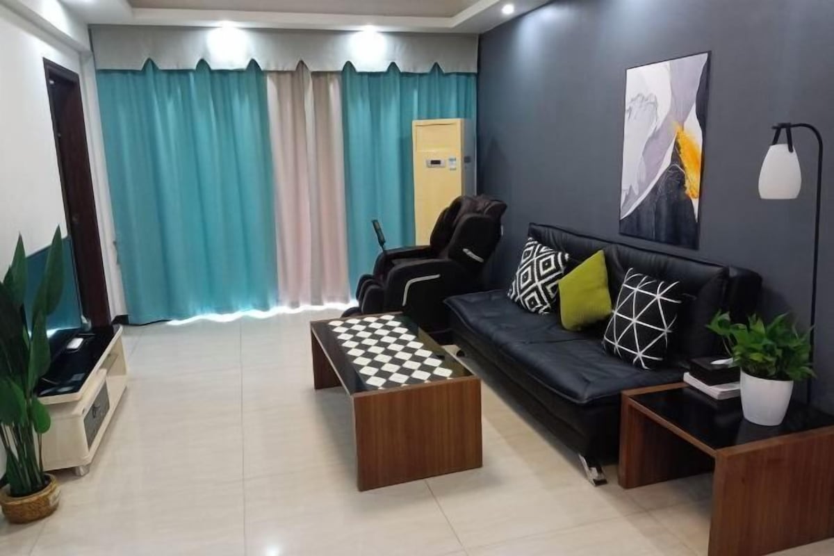 A modern living room with a black sofa, patterned cushions, a wooden coffee table, and a chessboard.