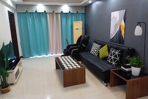 Ein modernes Wohnzimmer mit einer schwarzen Couch, gemusterten Kissen, einem Holztisch und einem Schachbrett.