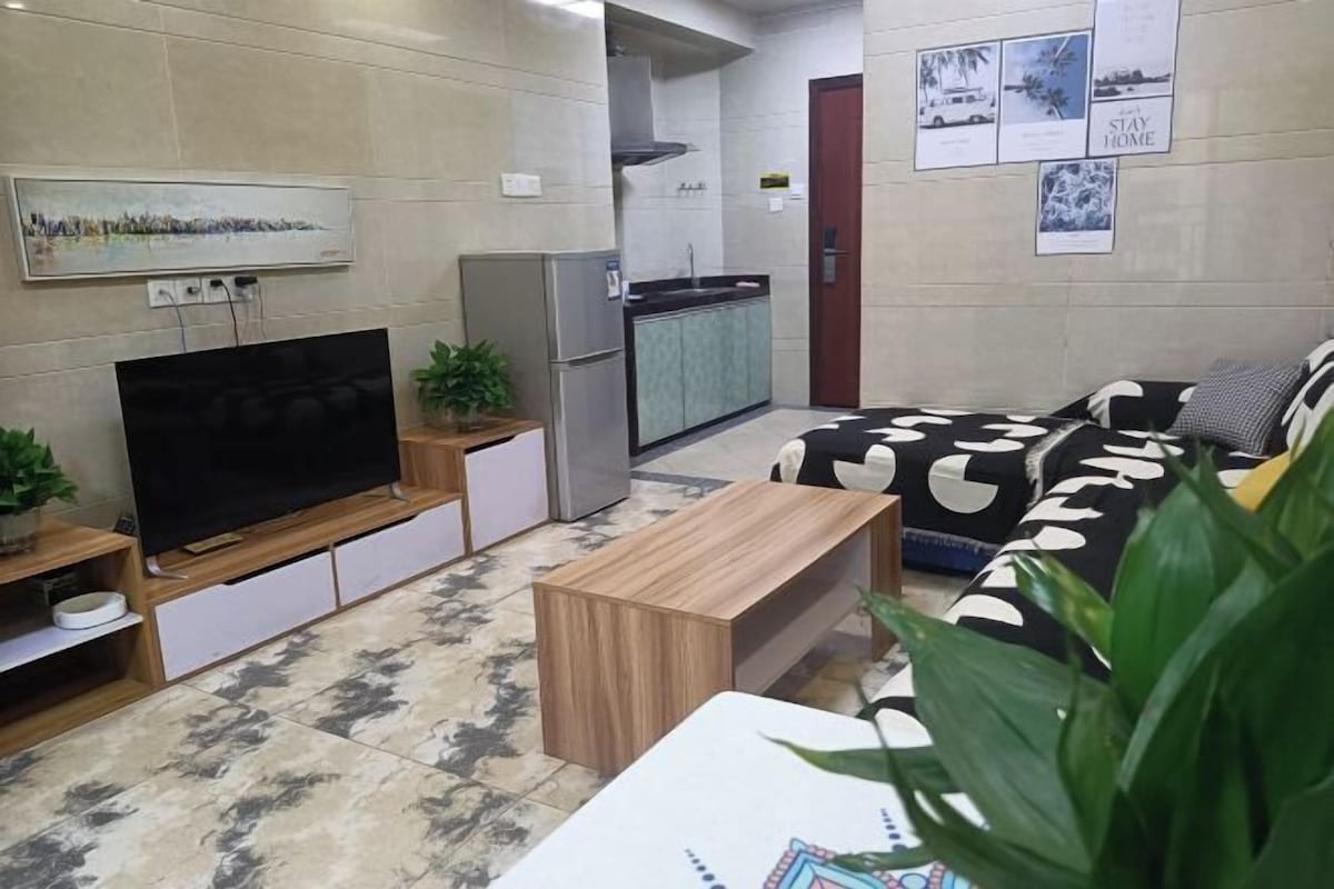 A living room with a TV, sofa, coffee table, and kitchen area.